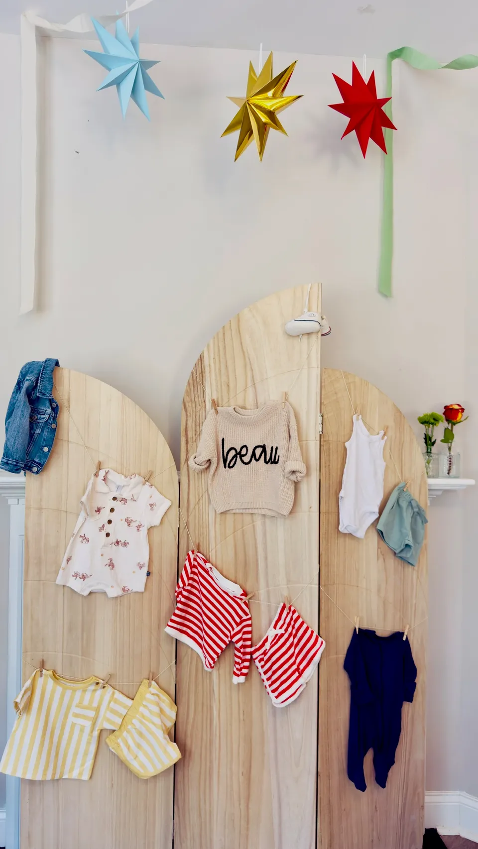 Baby shower display of tiny outfits hung across wooden panels