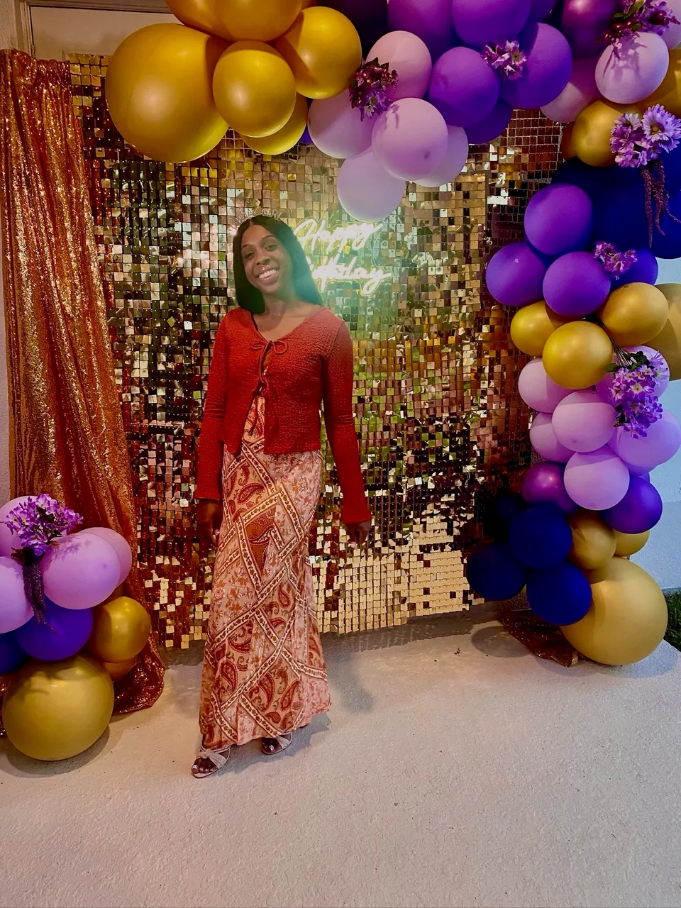 Guest posing before a sequin backdrop framed by gold and purple balloons